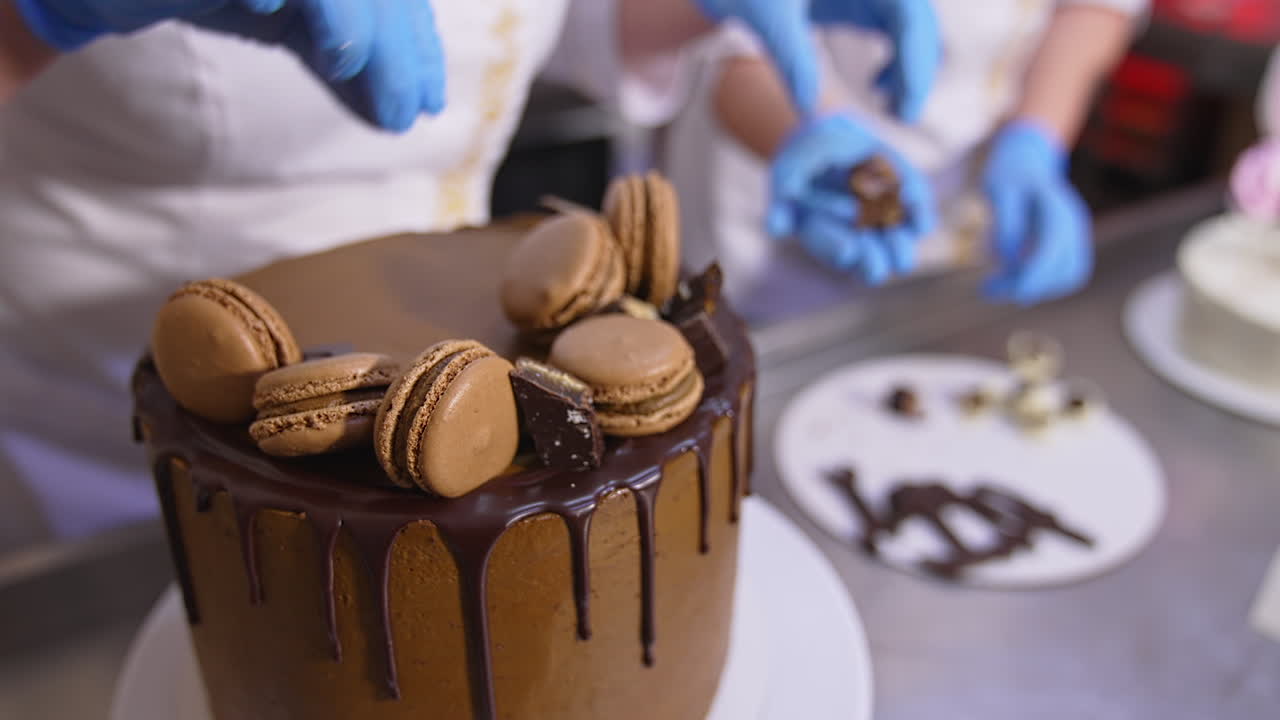 Tasty chocolate cake beautifully decorated in the food factory. Pastry professionals put the sweets on top of the big cake. Close up.