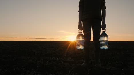person carrying water bottles at sunset in a field