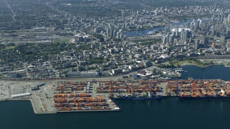 Container Ships Load Cargo At Centerm Shipping Terminal Along Vancouver Harbor Waterfront With City Skyline Behind In Vancouver, Canada. - aerial shot