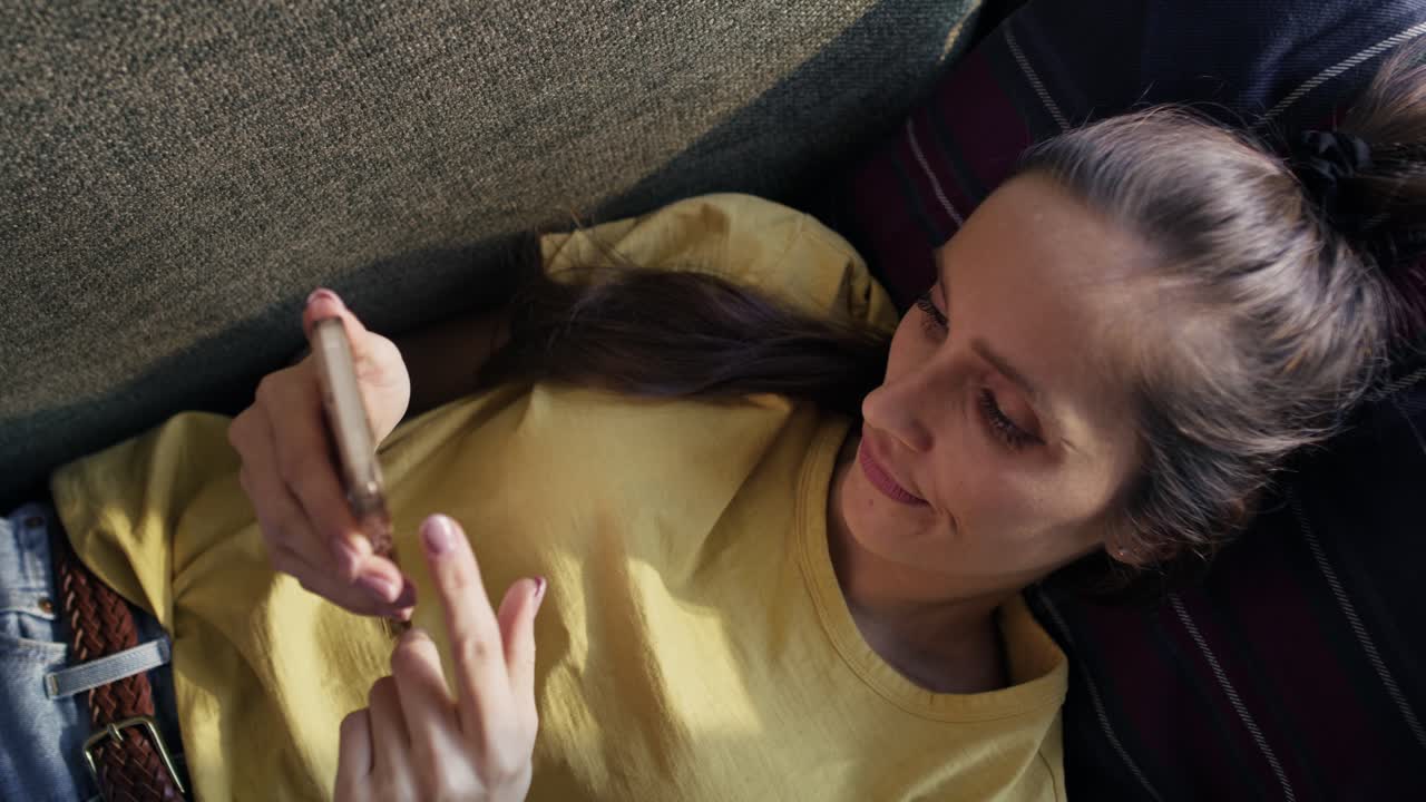 vista superior de una mujer caucásica acostada en el sofá y navegando por teléfono