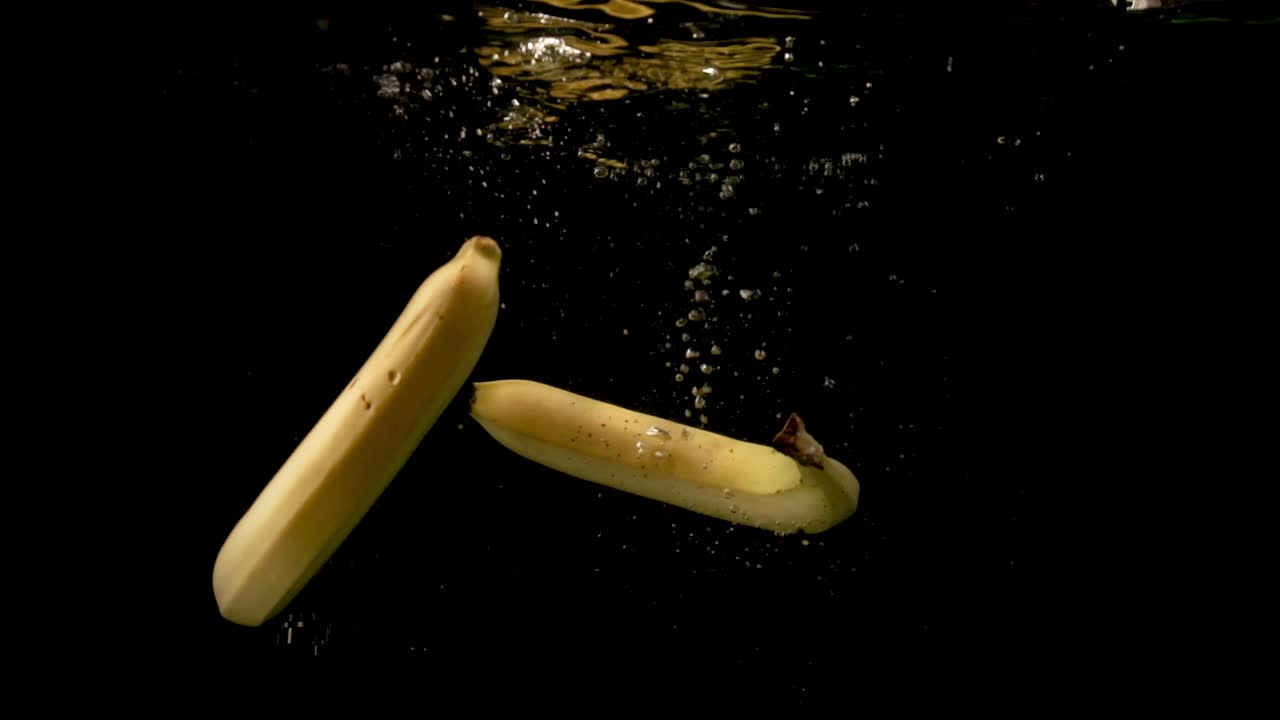 맑은 어두운 물에 떨어지는 육즙이 많은 노란색 신선한 바나나