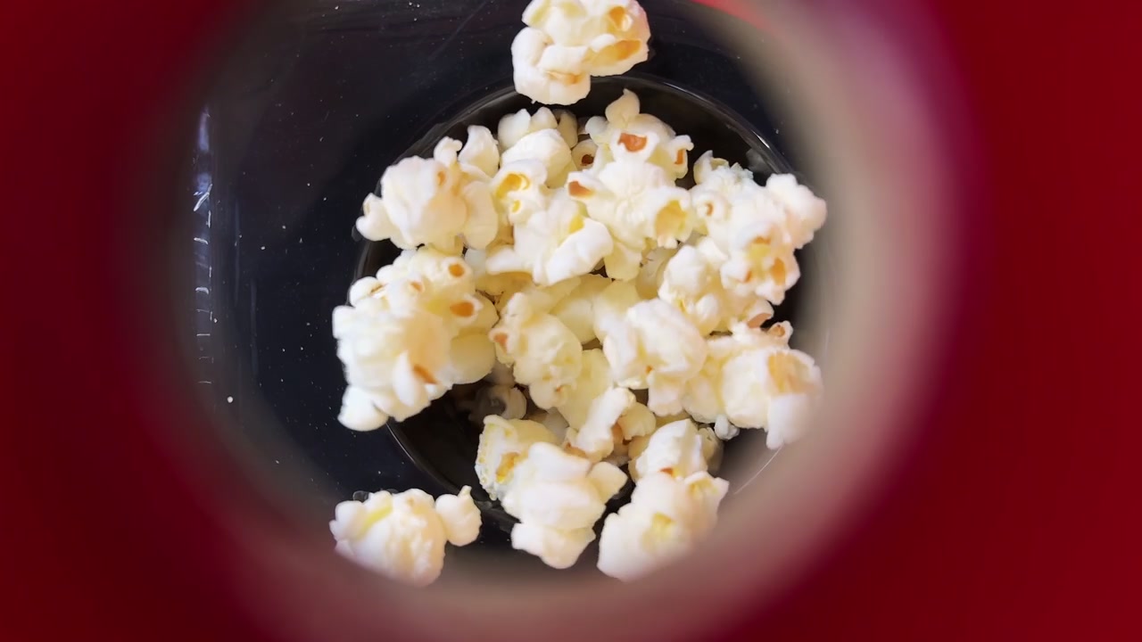 Una creativa ripresa ravvicinata dall'alto di chicchi di popcorn bianchi freschi all'interno di una macchina. Prospettiva POV circolare unica, perfetta per snack da cinema, video di cucina e pubblicità dell'industria alimentare