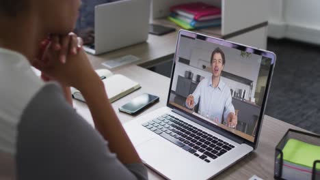 sección media de una mujer afroamericana haciendo una videollamada con un colega masculino en una computadora portátil en la oficina