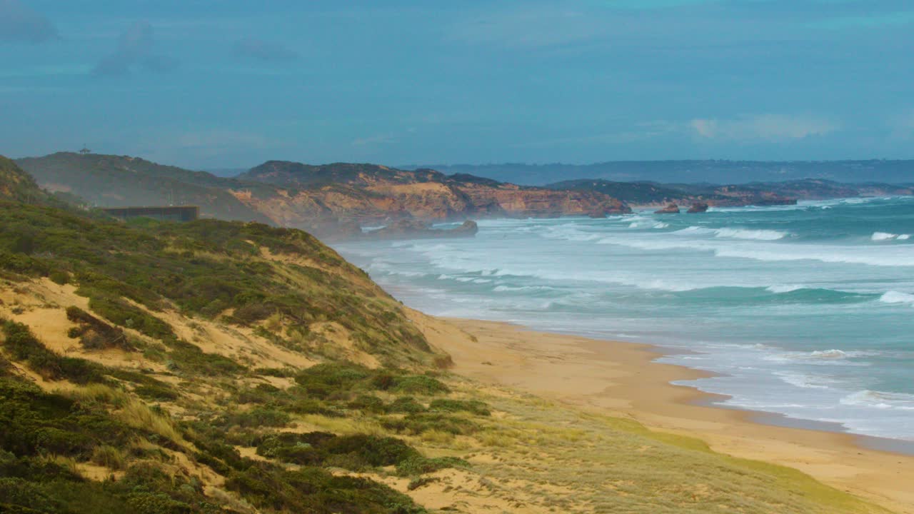Wide shot pans along rugged limestone cliffs, sandy beach, and turquoise ocean under daylight