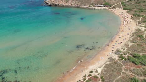 aerial footage of a busy beach in malta with clear turqouise mediterranean sea
