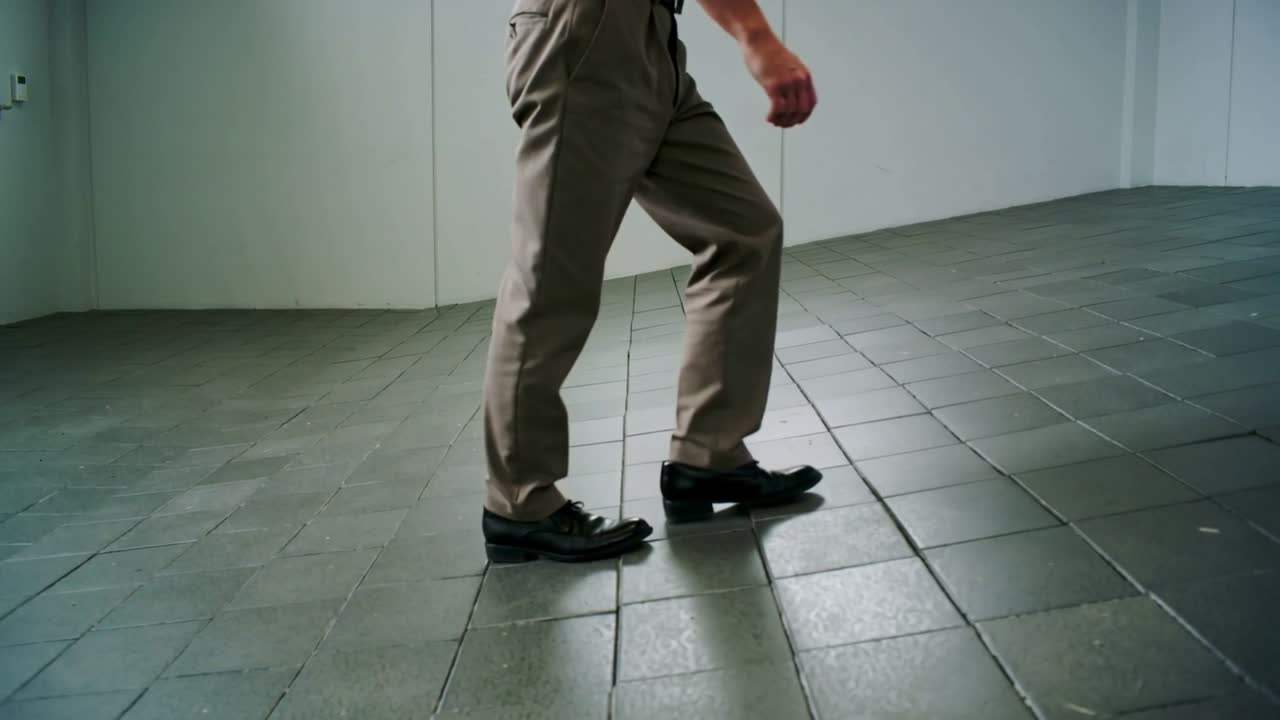 Eintretender erwachsener Mann geht in einem Raum über Fliesenboden, trägt Khakihose, dunkle Schuhe, mit Kopierraum.