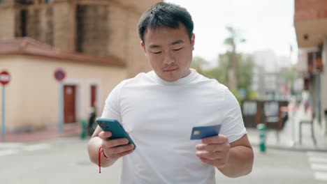 young chinese man using smartphone and credit card at street