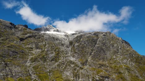 vista de ángulo bajo de nubes blancas volando sobre el pico de la montaña en el parque nacional fiordland de nueva zelanda en verano