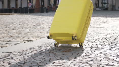 rear view of elegant woman walking in old city, pulling yellow suitcase. female tourist with bright yellow suitcase on old cobblestone. vacation in a european city