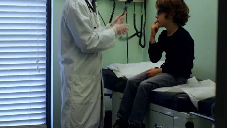 Side-view-of-young-asian-male-doctor-examining-a-caucasian-boy-patient-ear-with-tool-in-a-clinic-4k