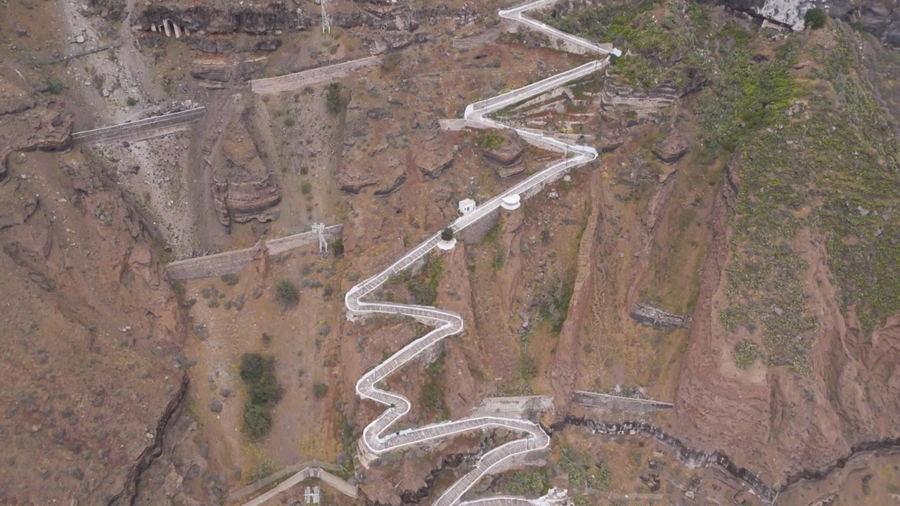 Ripide scale di Karavolades su scogliera vulcanica che collegano il Porto Vecchio a Fira sull'isola di Santorini in Grecia. Ripresa aerea in movimento.