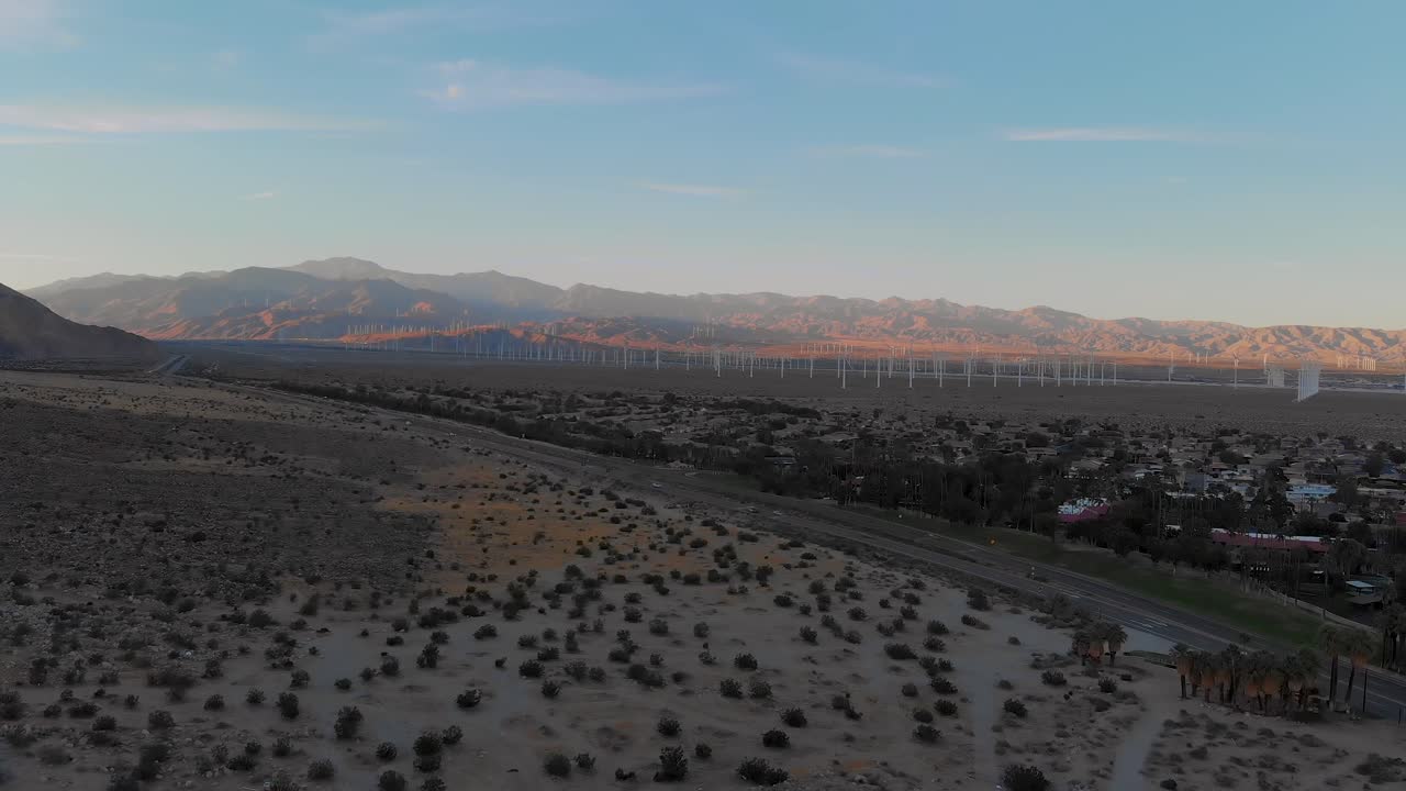 Ripresa aerea con drone: lento allontanamento sopra la vegetazione desertica, con mulini a vento fuori da una piccola città.