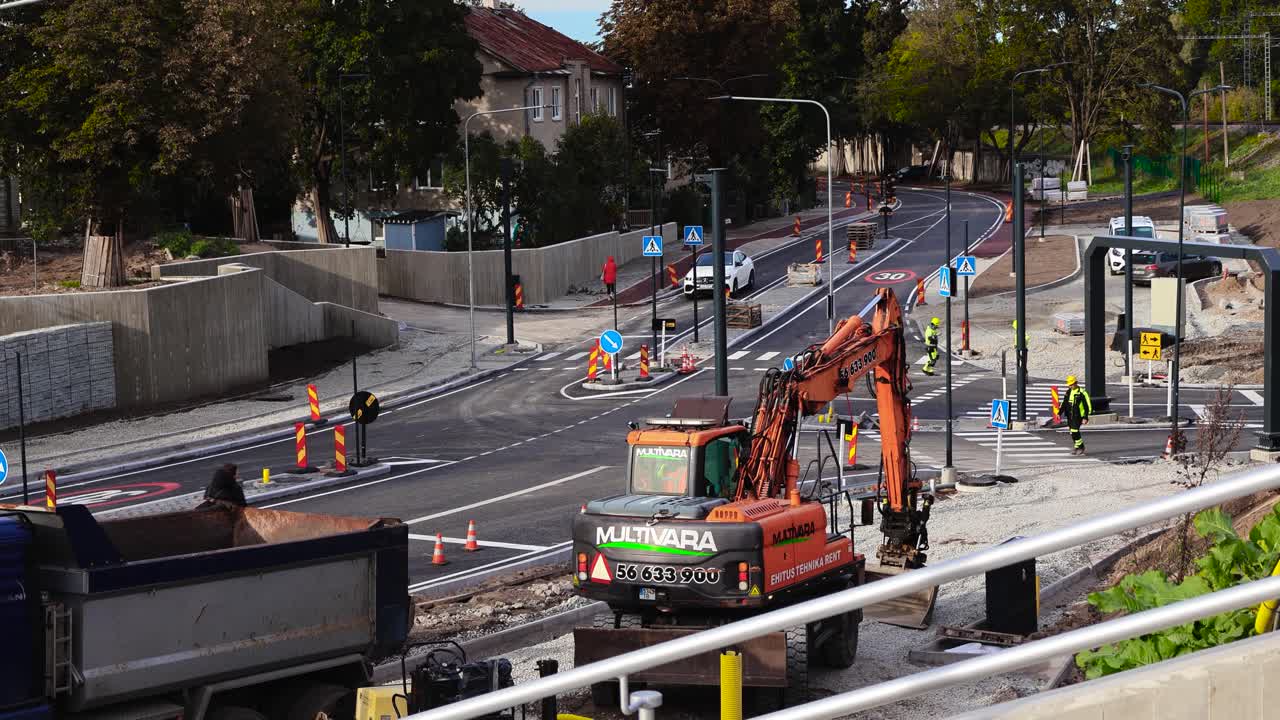 Road construction site at Kristiine Tondi intersection that is a bridge underpass for railroad and trains building. New asphalt has white road markings and construction vehicles and people working.