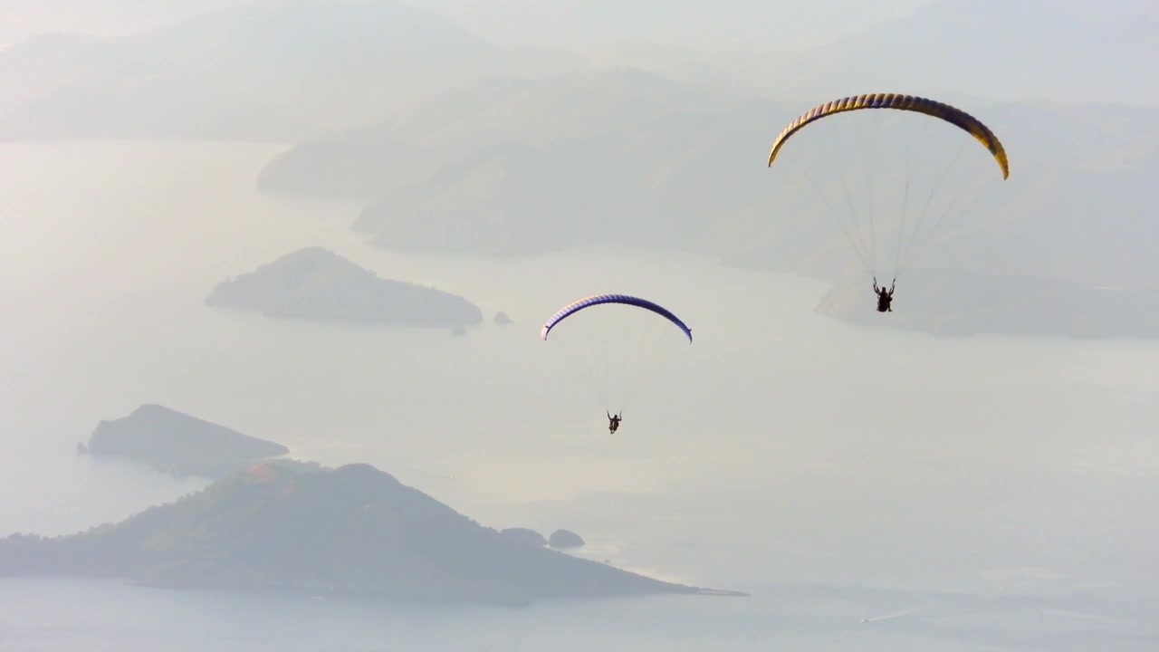Manzaralı bir kıyı şeridi üzerinde süzülen yamaç paraşütçüleri.