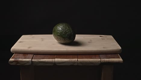 a ripe avocado lies quietly on a weathered wooden table, surrounded by darkness. subtle, directional lighting reveals its rich texture and earthy tones, creating a simple yet powerful visual