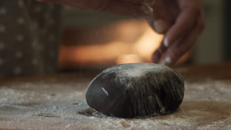 hand sprinkles flour on table and rolls gingerbread dough, close-up