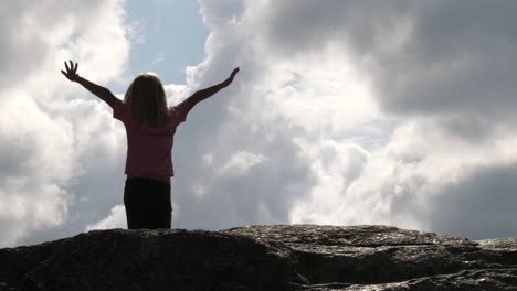 back view of child girl standing on rock and raising arms to the sky