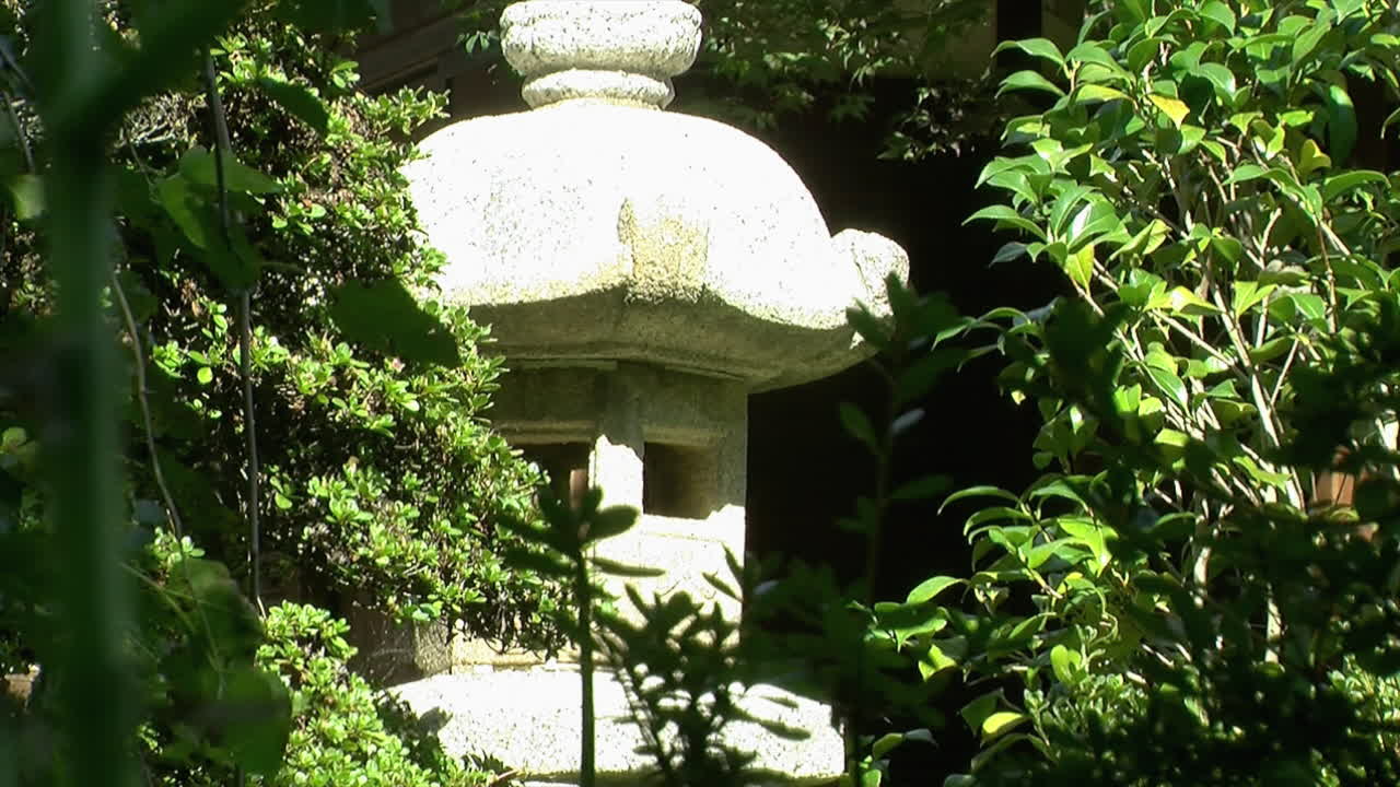 una linterna de piedra japonesa escondida entre plantas en un jardín japonés