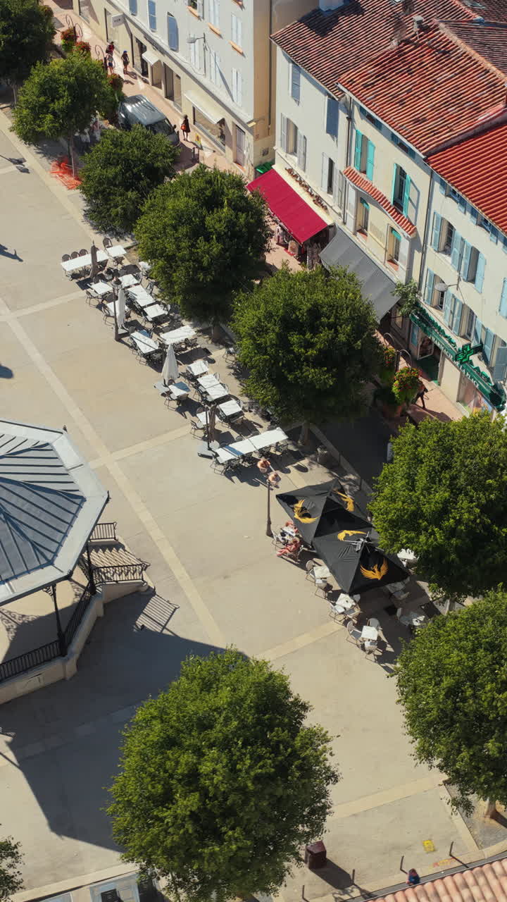 Aerial drone view of Place Nationale in Antibes, with trees, outdoor cafes, monument, and bandstand in the historic town center. Vertical