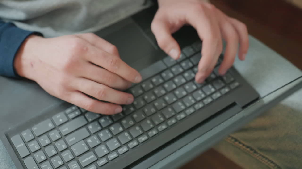 Close up hands typing on laptop, casual sweater on lap, indoor couch setting fiveframe sequence alternates roles as writer, coder, student, editor, freelancer with deliberate keystrokes, natural