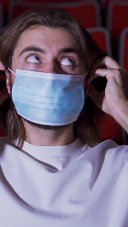 man wearing mask in a movie theater reacts to a scene