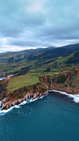 amazing picturesque rocks with greenery on the shore of the north atlantic ocean. aerial perspective on the stunning azorean islands. vertical video.