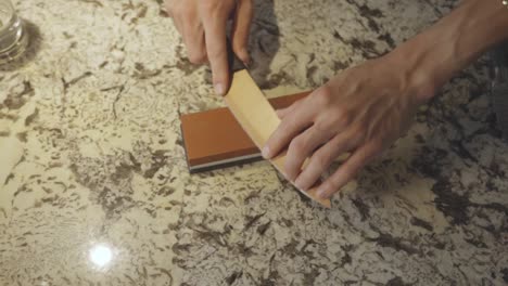 Kitchen-Knife-Being-Sharpened-With-Whetstone-On-Countertop