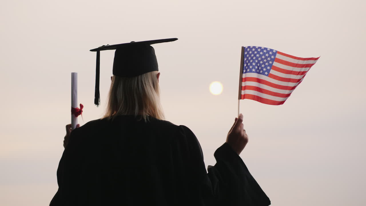 un estudiante con manto y gorra tiene un diploma y la bandera de los estados unidos estudia en américa