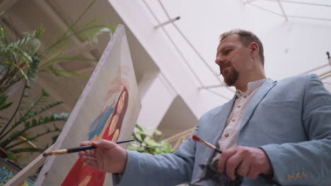 artist draws blue background on woman portrait in studio. concentrated painter applies color onto canvas imagining lady in red in workshop