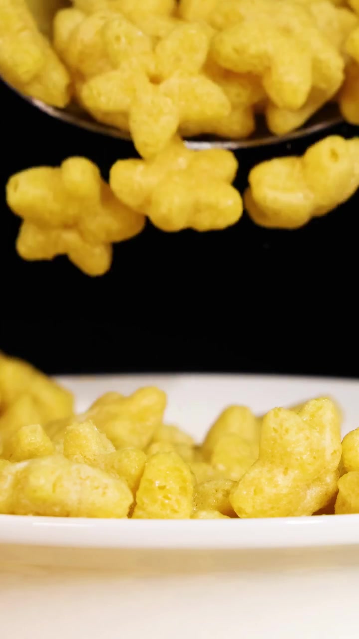 Cereali a forma di stella vengono prelevati e versati con un cucchiaio in una ciotola su sfondo nero