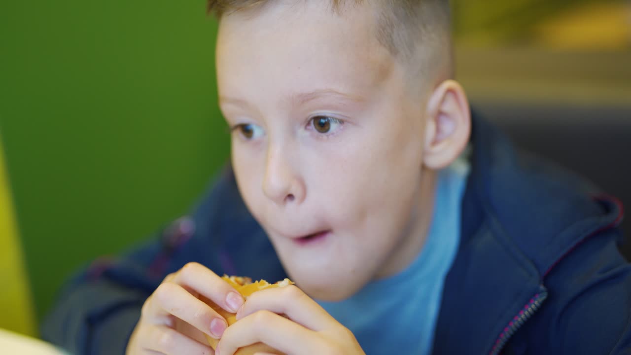 Young teenager eating tasty hamburger in fast food restaurant. Harmful nutrition