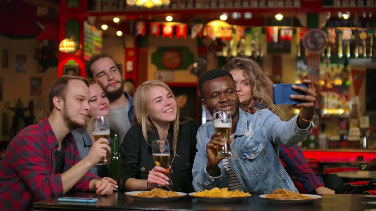 Friends are taking selfie with smartphone in bar. Young people are posing laughing and talking. Beer bottles and. Friends are taking selfie with smartphone in