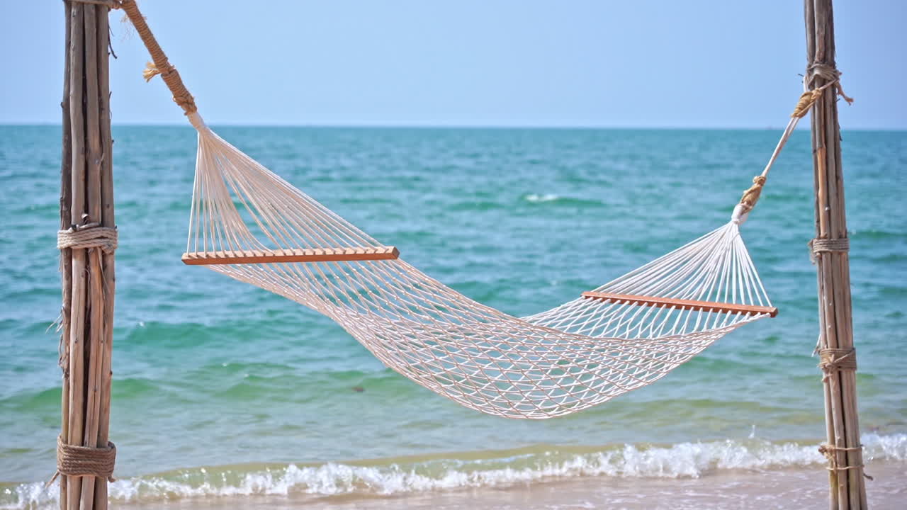 hamaca blanca vacía cuelga de los postes en la playa de la isla tropical con un mar turquesa tranquilo en el fondo y pequeñas olas que lamen en la playa de arena