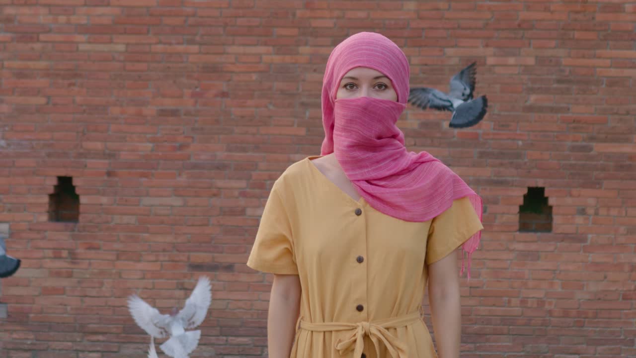 Woman in Pink Scarf and Yellow Dress in Front of Brick Wall