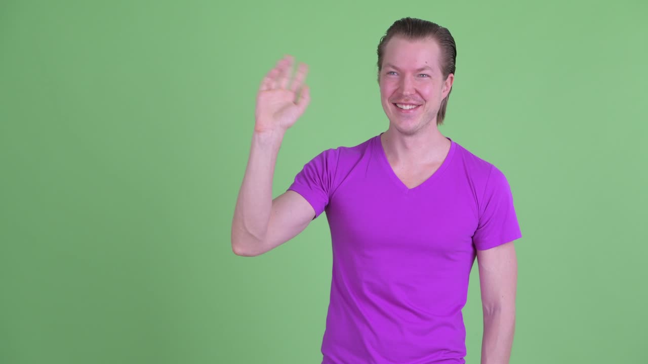 fotografía de estudio de un joven sonriendo y agitando la mano contra un fondo verde