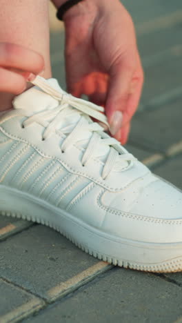 primer plano de una persona atando cordones de zapatillas blancas en un camino de pavimento entrelazado, centrándose en las manos ajustando firmemente los cordones para un ajuste seguro