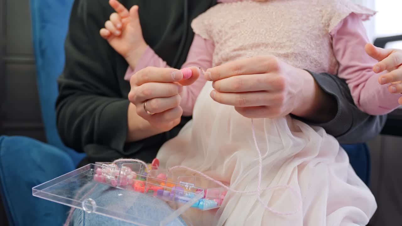 Father and daughter making bead necklaces, close up view