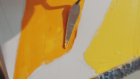 close up of applying yellow paint to canvas with palette knife