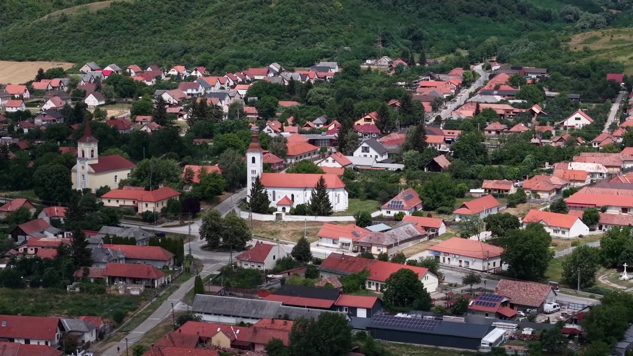 Tradiční domy a kostely osidlují idylickou evropskou vesnici zasazenou v bujném zeleném údolí, ukazující klidnou, malebnou krajinu.