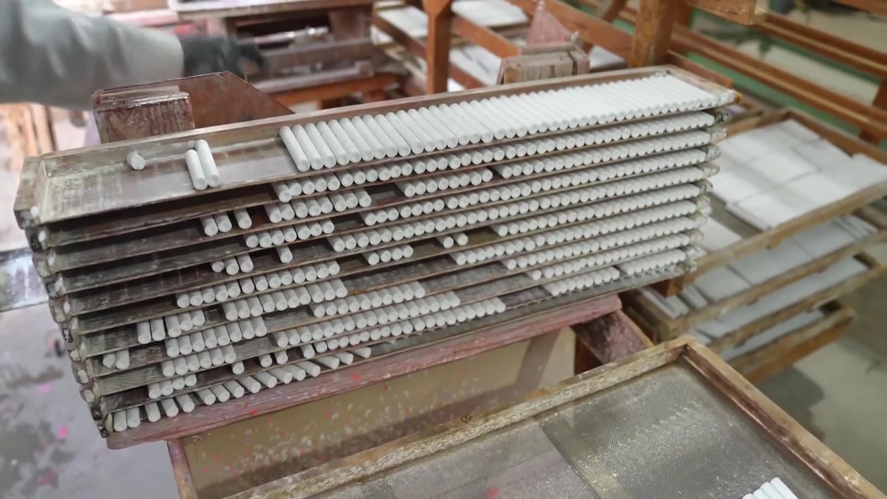 Operaio che impila telai di legno pieni di gessetti bianchi in fase di asciugatura in un laboratorio tradizionale di gesso.