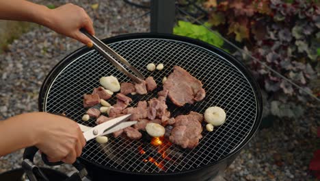 a close-up of woman's hands using kitchen scissors to cut grilled pork into bite-sized pieces on a charcoal grill, a traditional part of the korean barbecue (gogi-gui) dining experience