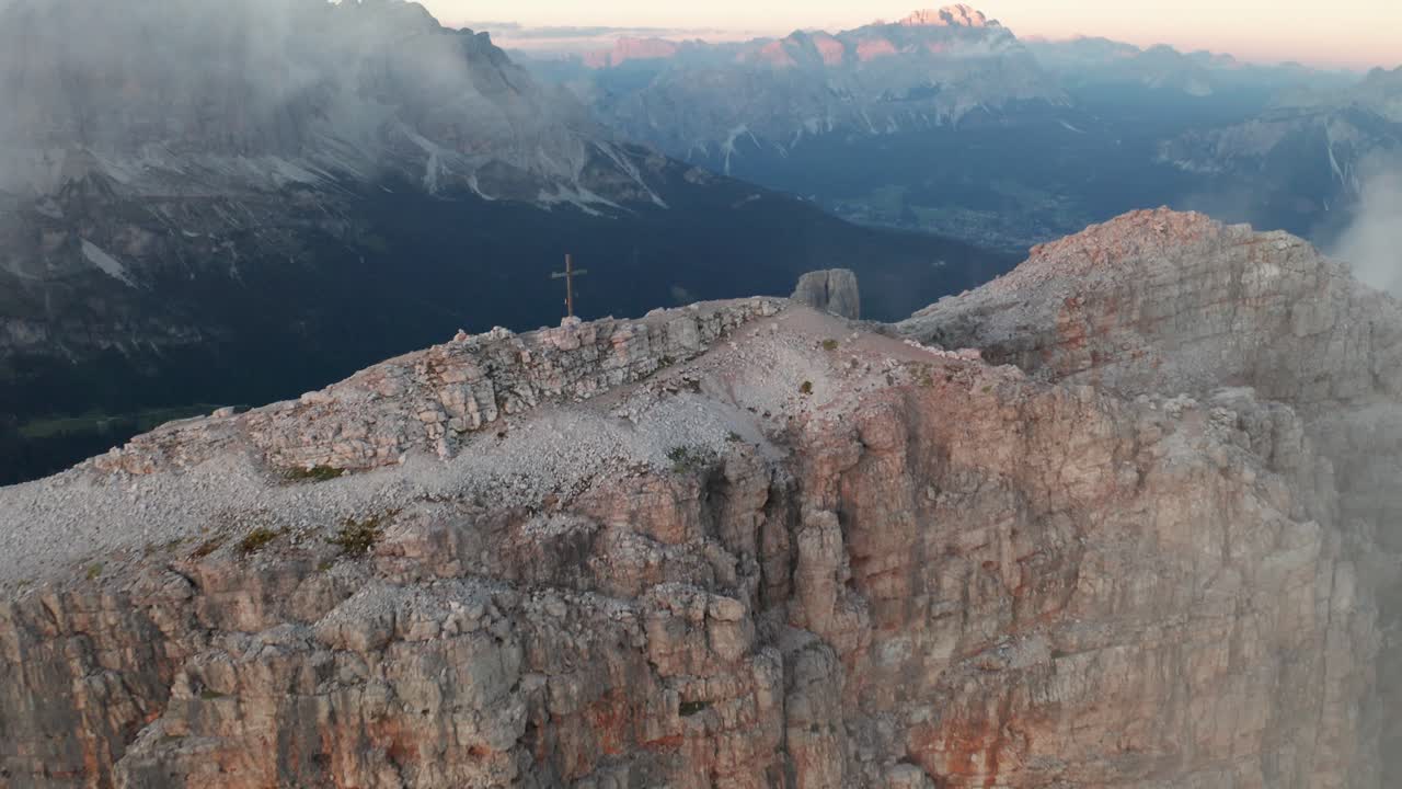 Ripresa aerea in avvicinamento della croce di vetta sulla cima del Monte Averau al tramonto - ripido pendio e valle