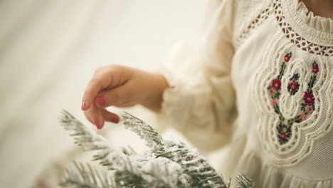 young girl caressing pine christmas ornament branch in white festive dress - close up