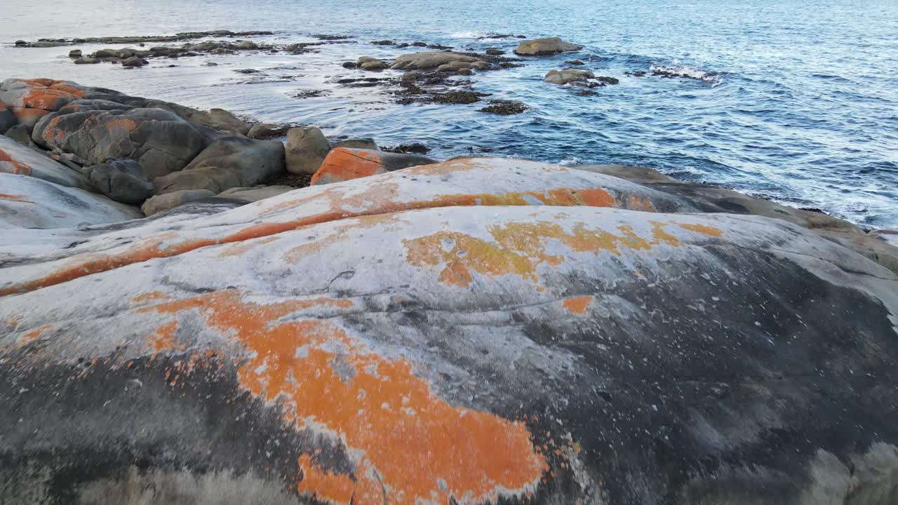 беспилотник движется вперед над заливом красных скал с разбивающимися волнами из голубого океана