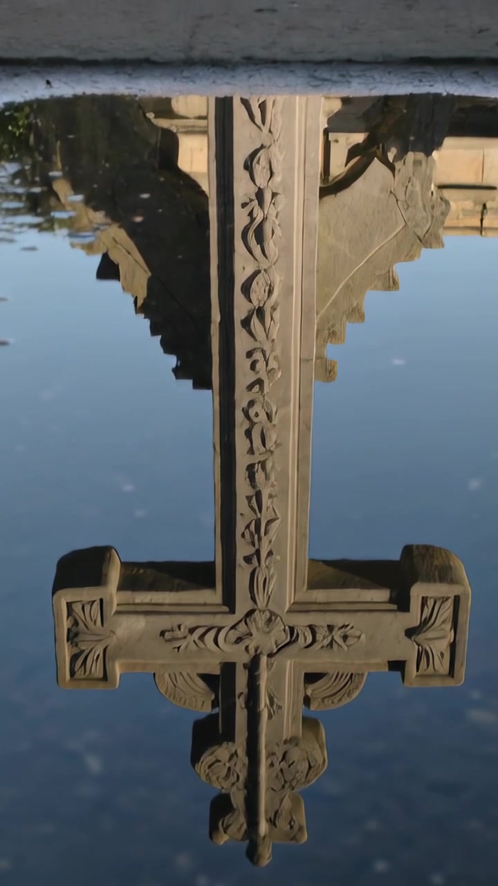 Video verticale: La telecamera si allontana rivelando il riflesso di una croce ornata in una vasca commemorativa, mostrando il bordo.