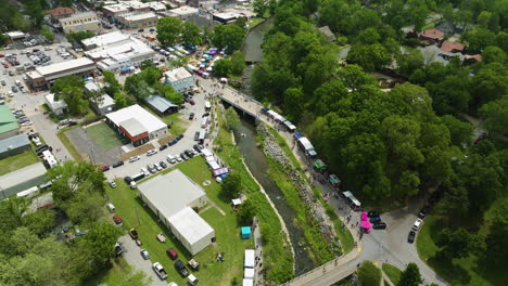 Booths-And-Parked-Cars-With-People-Gathering-By-The-Sager-Creek-During-50th-Dogwood-Festival-In-Siloam-Springs,-Arkansas