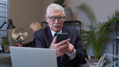 Senior-businessman-grandfather-with-smartphone-texting-checking-email-messages-online-at-work