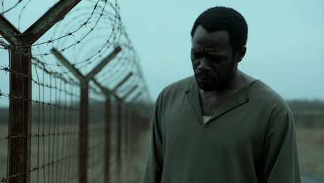 man standing beside a long barbed wire fence on a gloomy day