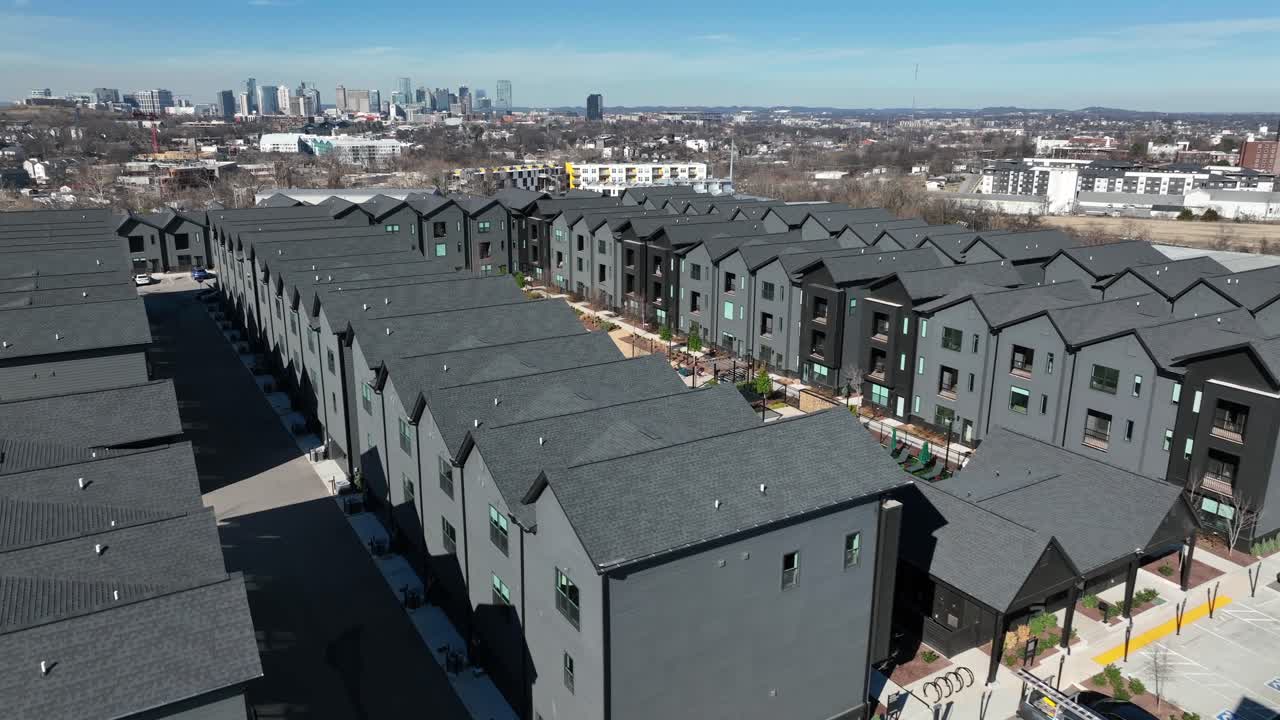 Luftfoto af solrig udsigt over moderne luksusboligområde i Nashville, Tennessee med moderne lejlighedsbygninger, anlagte gårdhaver med pool og byens skyline i baggrunden.