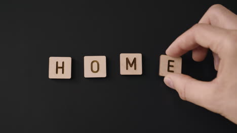 a close-up of a caucasian hand placing carved wood letters that form the word ''home'